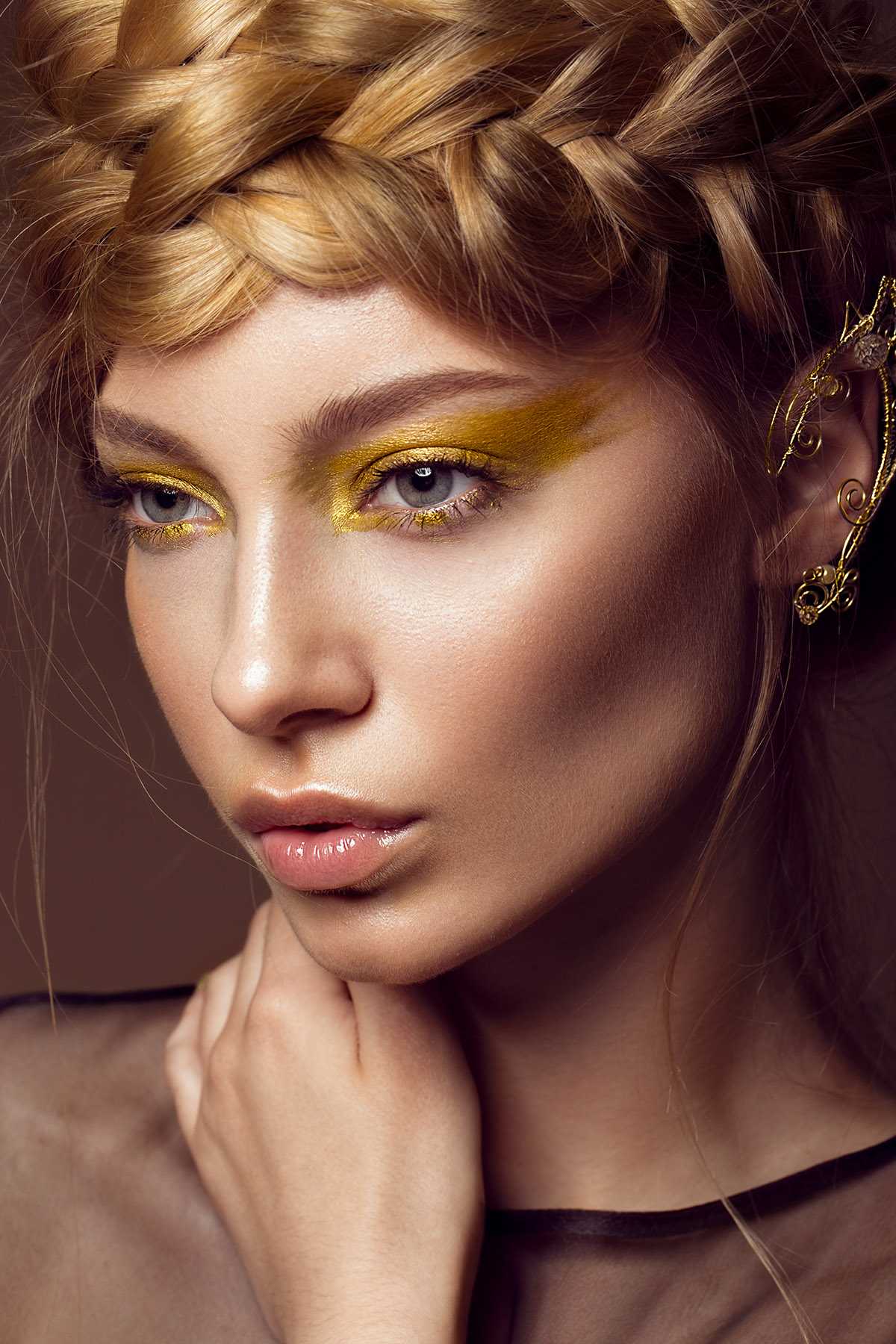 Beautiful girl in a gold dress with creative makeup and braids on her head. The beauty of the face. Photos shot in the studio.